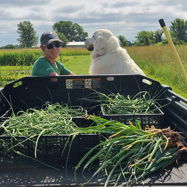 Hidden Mesa farmer sitting in an ATV with her dog next to her in the seat and vegetables in the bed of the vehicle Hidden Mesa farmer sitting in an ATV with her dog next to her in the seat and vegetables in the bed of the vehicle