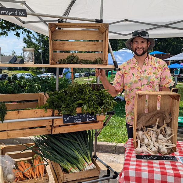 A man stands next to a display of vegetables under a tent A man stands next to a display of vegetables under a tent